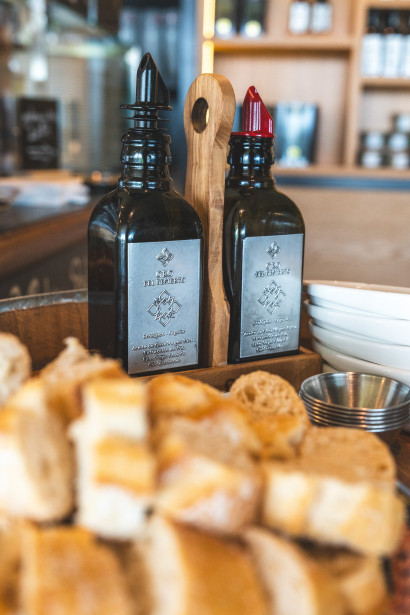 Two bottles of olive oil in a wooden holder, with small bowls and baguette cubes in front.
