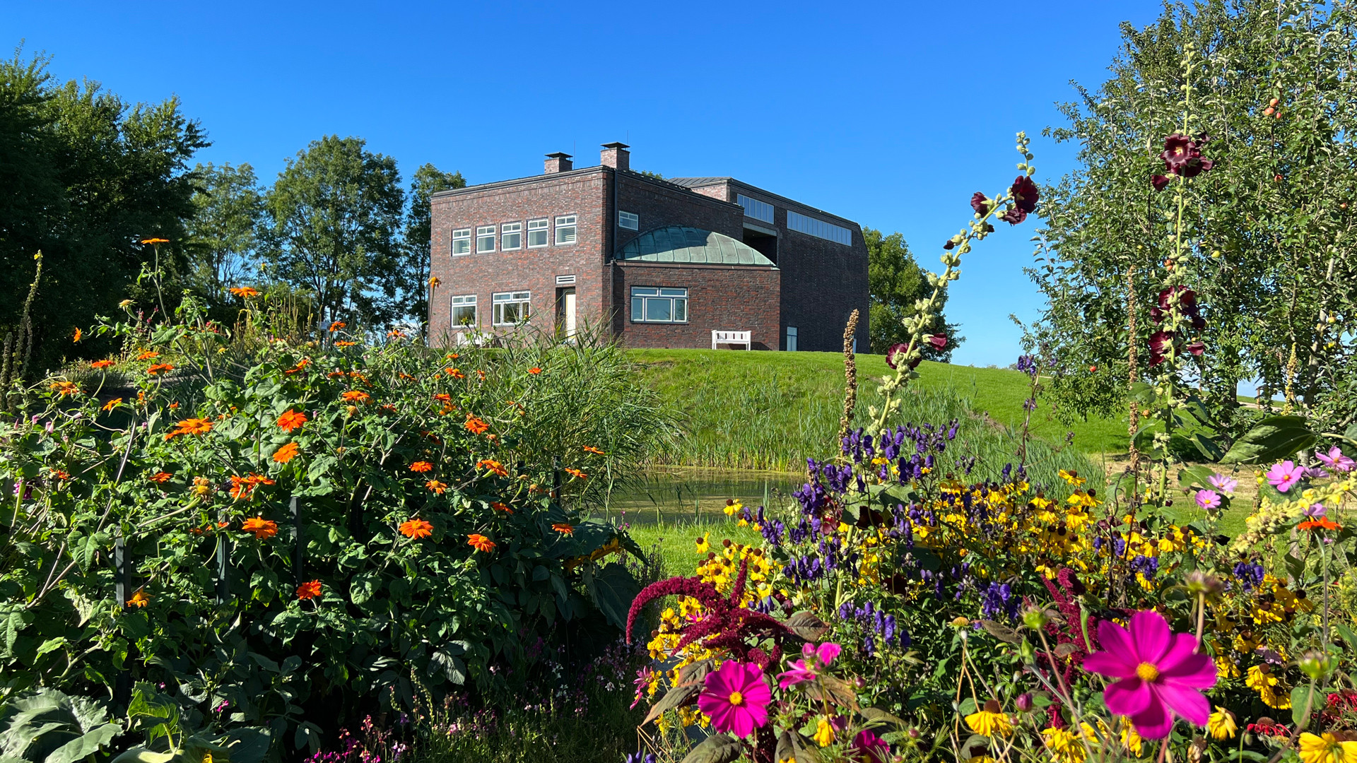 The Nolde House in Seebüll with Fething and the Nolde Garden in the foreground under a blue sky.