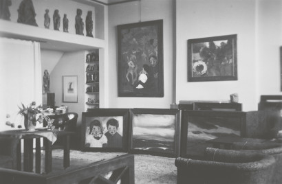 Wohnzimmer mit zahlreichen Werken Noldes an W&auml;nden und auf dem Boden, davor Couch, Sessel und Couchtisch.