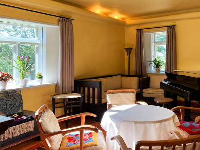 Sonnengelbes Wohnzimmer im Nolde-Haus mit originaler Einrichtung, darunter runder Tisch, St&uuml;hle, Couch, Sessel und Fl&uuml;gel.