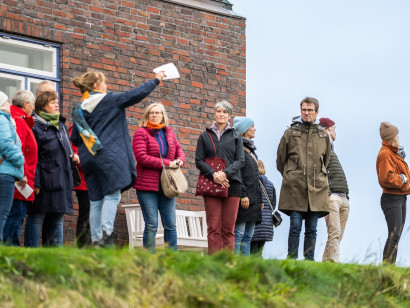 Guided group of visitors in autumn clothing standing in front of the Nolde House, attentively looking towards the Nolde Garden and Botanicum.
