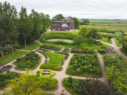 Aerial view of the Nolde House with its green garden and the surrounding marshland on a bright, cloudy late-spring day.